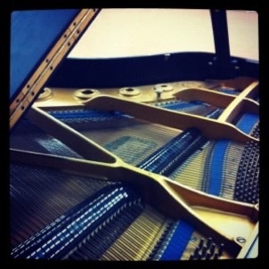 A Kawai grand piano with the lid open so you can see the strings, dampers, and gold-painted iron frame. 